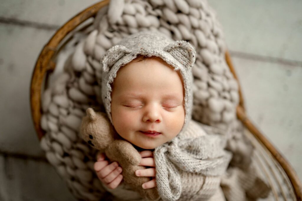 Baby holding teddy bear while wearing bear hat during Columbia MD Newborn Photo Session