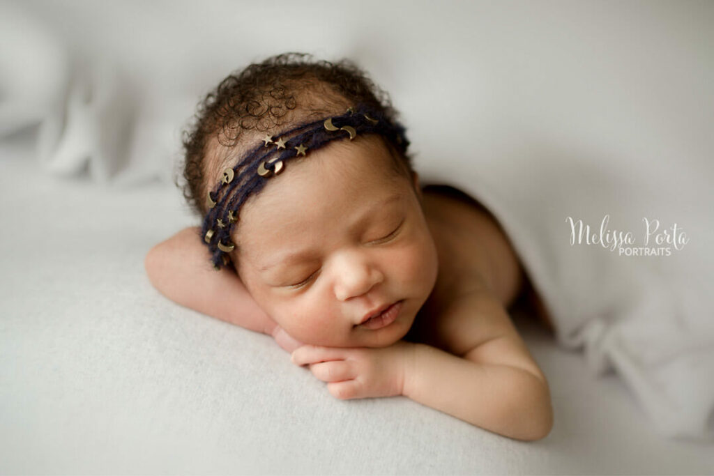 Baby girl posed while sleeping featuring navy moon and stars headband during her newborn photography session in Columbia, MD