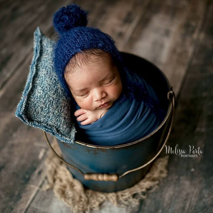 Baby boy wrapped in navy blues in matching bucket during his newborn photography session in Clarksville, MD