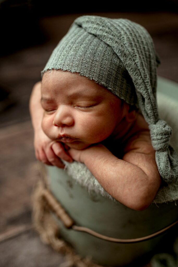 Newborn sleeping in bucket in seafoam green with hat during Baltimore Newborn Photography Session
