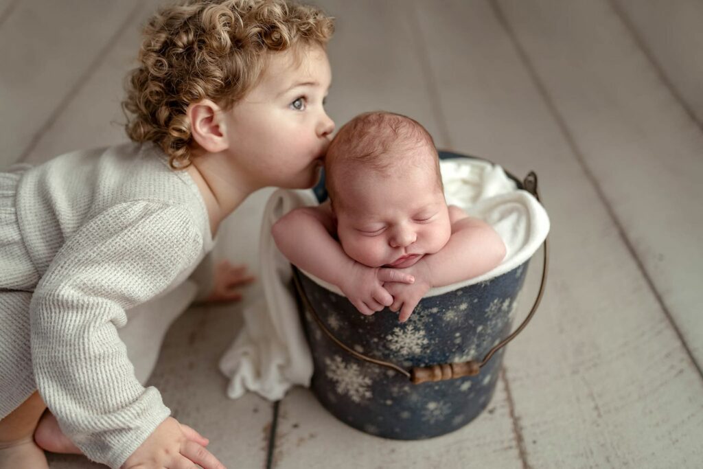Big sister kissing her new baby sibling during her Newborn Photography Session in their Sykesville, MD home