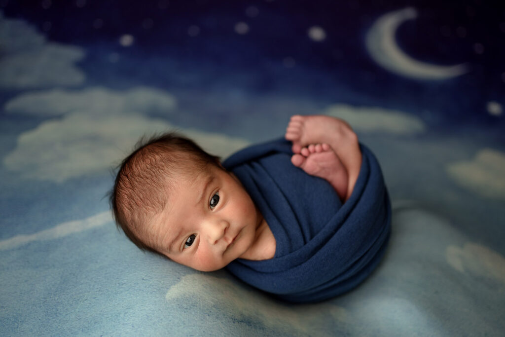 Awake baby boy on cloud and moon nighttime backdrop during his Clarksville, MD Newborn Photography Session