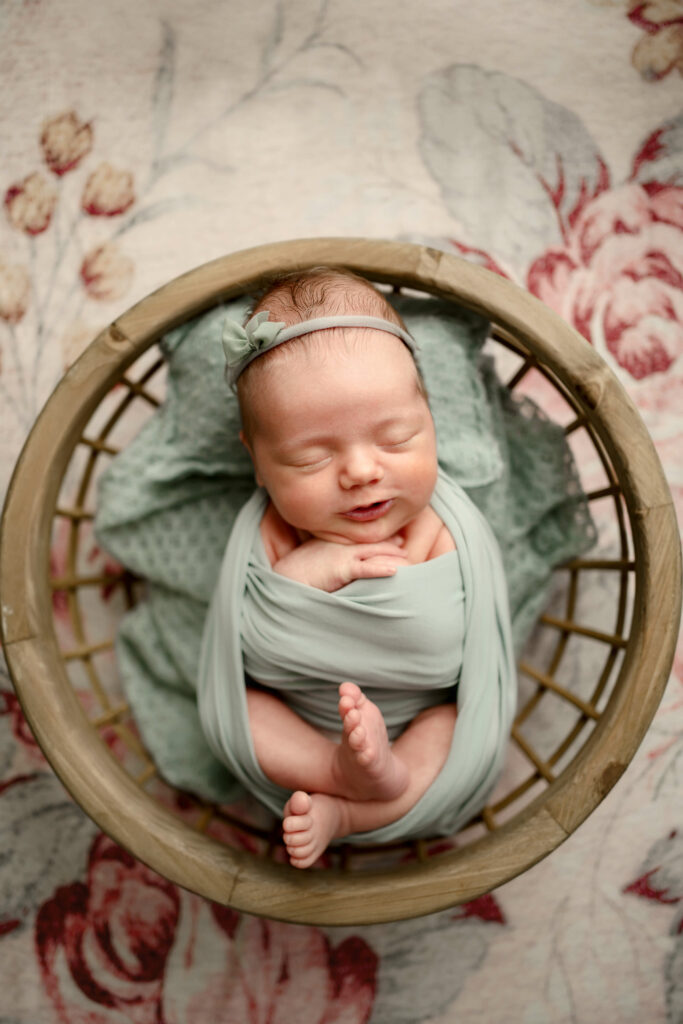 Baby sleeping in a bowl on a pink floral background during her Ellicott City Newborn Photography Session