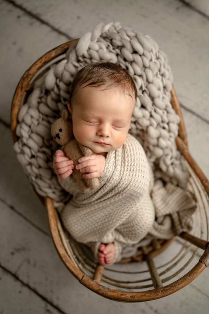 Baby wrapped in a basket holding a tiny stuffed bear during his photo session in his Columbia, MD home