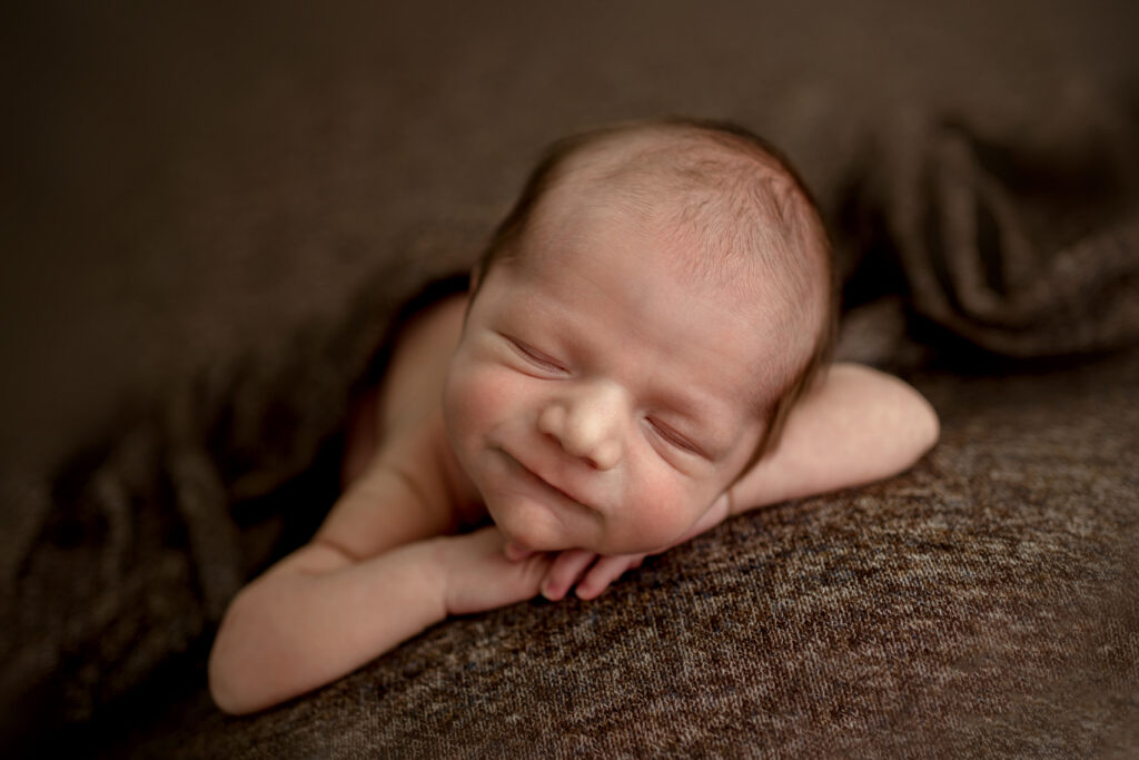 Columbia MD Newborn Baby boy smiling while sleeping on a brown backdrop