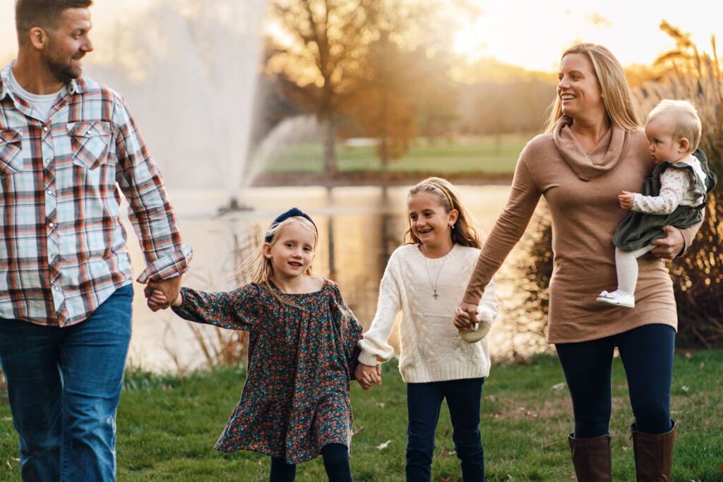 Loving family laughs while holding hands in front of Turf Valley Pond during a golden hour sunset session
