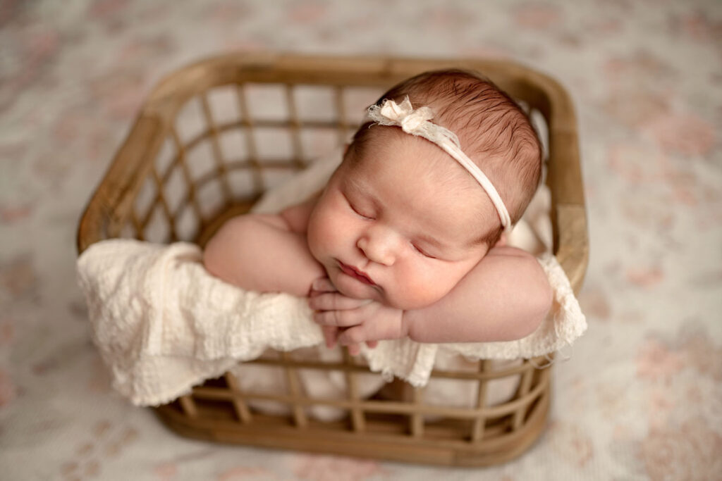 newborn baby girl posed in basket with a floral backdrop