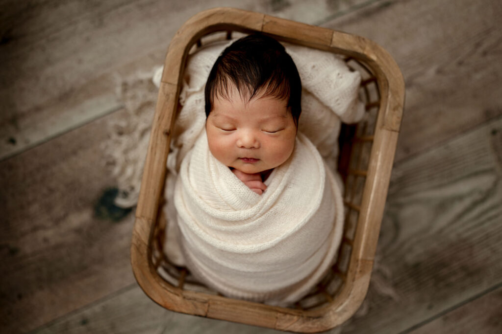 baby wrapped in a rectangular rustic wooden basket