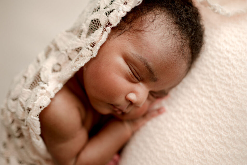 newborn curled up in womb pose draped with pink lace