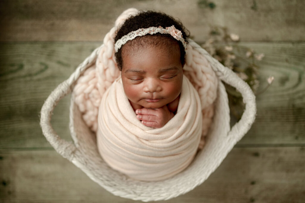 Baby wrapped in soft pinks in a white basked for an in-home newborn photo session